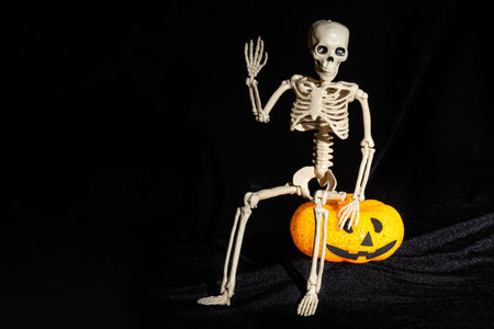 Skeleton sitting on a lamp in the shape of a pumpkin with a grin and waving his hand in greeting on...