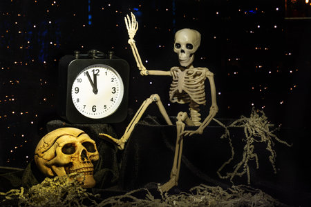 A skeleton waking up, crawling out of the grave and turning off the alarm clock, a skull on a black background with stars. The eve of the day of death. It's Halloween time.の写真素材