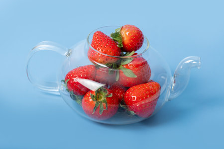 Glass transparent teapot full of red ripe strawberries on a blue background. Summer is a healthy drink. Summerberry tea. Healthy fruit drinks. Berry background.の写真素材