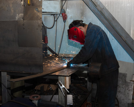 A male worker in uniform cutting a metal part with a cutter at the workplace at the factory. Sparks,...
