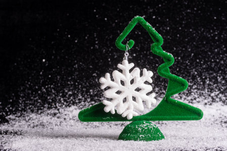 Creative little green Christmas tree with a hanging white snowflake on a black snowy background, minimalism. waiting for a miracle. New Year and Christmas cardの写真素材