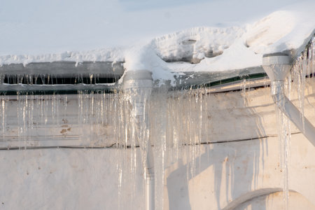 Icicles hanging from the roof of the house. Melting snow on the roof. Dangerous sharp transparent...