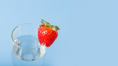 A glass glass with water and red ripe strawberries isolated on a blue background. Summer is a healthy drink. Summer cocktail Healthy fruit drinks. Women's Sweet Natural Drinkの写真素材