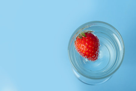 A glass glass with water and red ripe strawberries isolated on a blue background, top view. Summer is a healthy drink. Summer cocktail. Healthy fruit drinks. Womens Sweet Natural Drinkの写真素材