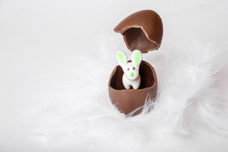 White Easter Bunny in a cracked chocolate egg and a flying empty eggshell in a nest of white...