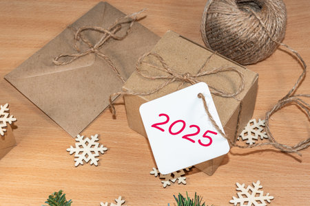 Happy New Year 2025. Eco-friendly gifts, homemade gifts, DIY. Gifts made of craft paper with the label 2025 on the table with wooden snowflakes, rope, envelopeの写真素材