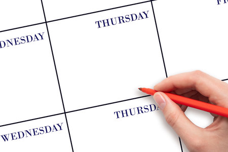 THURSDAY. Hand holding red pen writing in blank Thursday cell of a weekly calendar layout on clean white background, planning or scheduling concept. Save the date. Holiday.  Important date.の写真素材