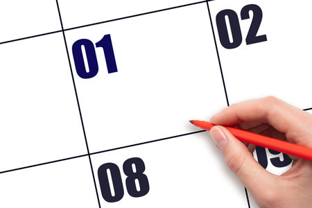 Calendar date 1. A hand holding a red pen is about to write text on an empty white calendar page with the date 1 without a month. Planning or scheduling concept.の写真素材