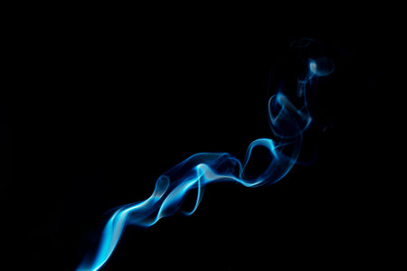 Wispy blue smoke wave flowing against a black background, creating a sense of mystery and elegance. Abstract and atmospheric concept. Swirling, writhing smoke to overlay on your photos.の写真素材