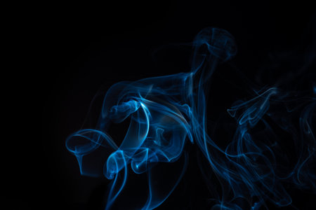 Wispy blue smoke wave flowing against a black background, creating a sense of mystery and elegance. Abstract and atmospheric concept. Concept of mystery and creativity to overlay.の写真素材