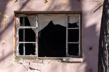Broken window frame with peeling paint exposes the dark interior of an abandoned structure, highlighting themes of urban decay and neglectの写真素材