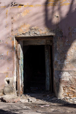 Abandoned doorway leads into a dark interior of a derelict structure with peeling paint and crumbling walls, illustrating urban decay and neglectの写真素材