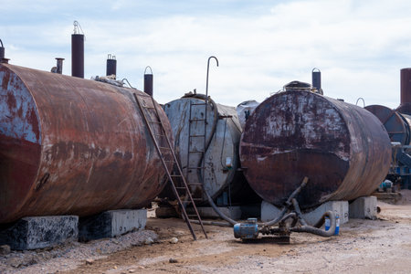 Large rusty fuel storage tanks with pipes and metal ladders in an outdoor industrial area, under daylight sky, concept of heavy industry decayの写真素材