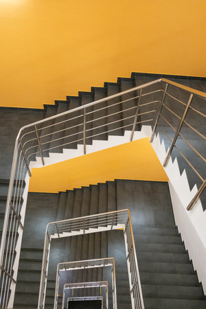 Spiral staircase features gray steps and a stainless steel railing, leading upward toward a bright...