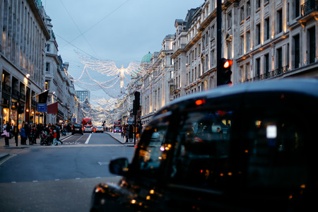 Traditional black taxi waits on a traffic light under twinkling Angel Christmas lights in Regent Street, London on Christmas Day.のeditorial素材