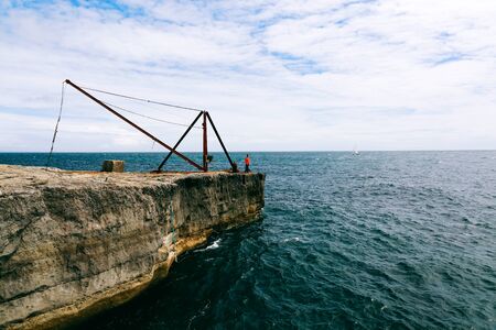 Young man stands on the rock with rusty steel fisherman's crane near Portland Bill Lighthouse on...