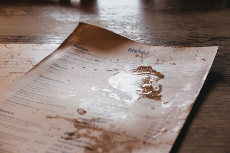 Pub menu with wine and beer stains on a wooden table in a traditional English pub.のeditorial素材