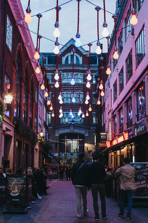 People walking under lightbulb lights in Carnaby Street, pedestrianised shopping street in Soho with over 100 shops and restaurants.のeditorial素材