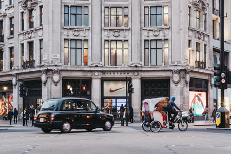Black cab and rickshaw passing in front of Nike Town, Nike's flagship store and the largest sports clothing and footwear department in Europe.のeditorial素材