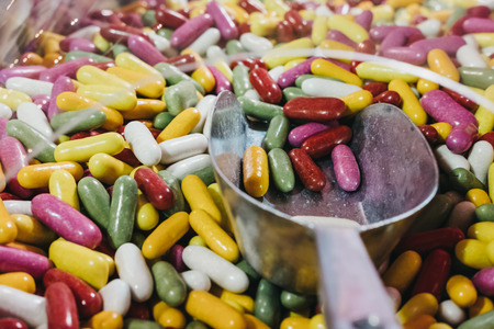 Hand with a metal scoop picking up multi-coloured jelly beans