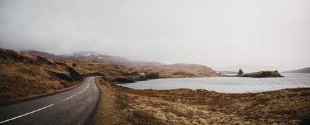 Road going through Scottish Highlands near Lochinver on a foggy spring day.