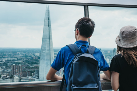 Rear view of people standing on an open air balcony in Sky Garden, London, looking at the Shard. Sky...