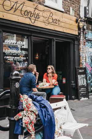 People sitting at outdoor tables of Monty's Bar in Brick Lane, one of the most popular tourist sites in London, UK.のeditorial素材