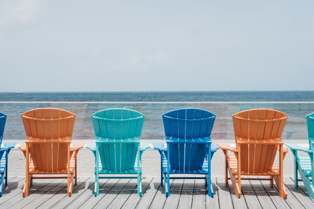 Rear view of the colourful deck chairs arranged in a row by the sea.の写真素材