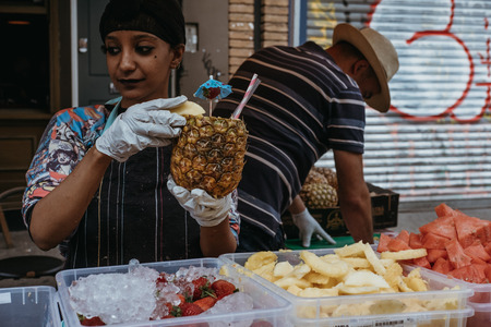 London, UK - July 21, 2018: Woman preparing a tropical drink served inside a fresh pineapple at a market stall in Portobello Road Market, one of the most popular tourist sites in London, UK.のeditorial素材