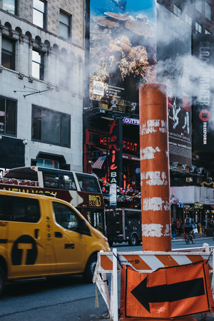 New York, USA - MAY 30, 2018: Yellow taxi drives past the steam vapour orange and white stack....
