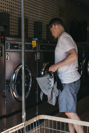 New York, USA - May 30, 2018: Man loading clothes in a washing machine inside laundromat in New York, the city where most locals donât have the advantage of in-unit washers and dryers.のeditorial素材