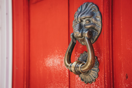 Close up of a lion's head door knocker on a bright red door of a typical British house.の写真素材