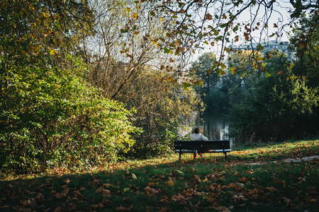 London, UK - October 27, 2018: Person sitting on a bench, relaxing by the pond in Hampstead Heath. Hampstead Heath covers 320 hectares one of London's most popular open spaces.のeditorial素材