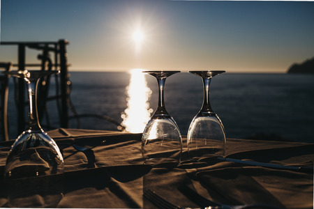 Empty wine glasses on the table by the sea, water and sunset on the background.