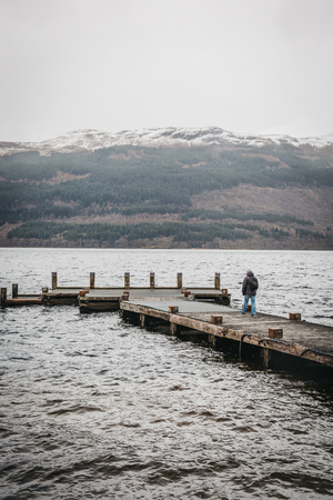 Loch Lomond, Scotland - March 17, 2018: Man walking on a pier on Loch Lomond in Scotland. The Loch forms part of the Loch Lomond and The Trossachs National Parkのeditorial素材