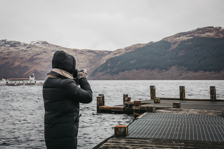 Loch Lomond, Scotland - March 17, 2018: Man taking photos on a pier on Loch Lomond in Scotland. The Loch forms part of the Loch Lomond and The Trossachs National Park.のeditorial素材