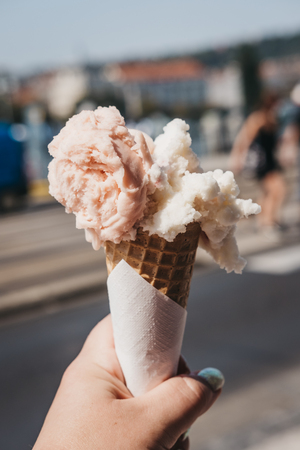 Colourful ice-cream in a wafer cone held in woman`s hand, blurred city on the background.