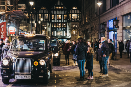 London, UK - January 05, 2019: People walking past black cabs parked on Argyll Street, London, Liberty of London department store on the background. Black cabs are an iconic symbol of London.のeditorial素材