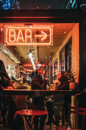 London, UK - January 26, 2019: People by illuminated window and neon sign on Bar in Canary Wharf on a rainy evening. Canary Wharf is a busy financial area of London that often host events.のeditorial素材