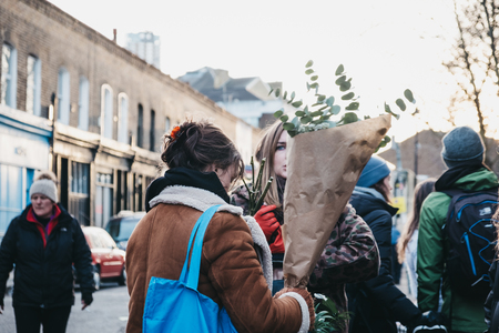 London, UK - February 03, 2019: People walking on a street with flowers purchased at the Columbia Road Flower Market, a street market in East London that is open every Sunday.のeditorial素材