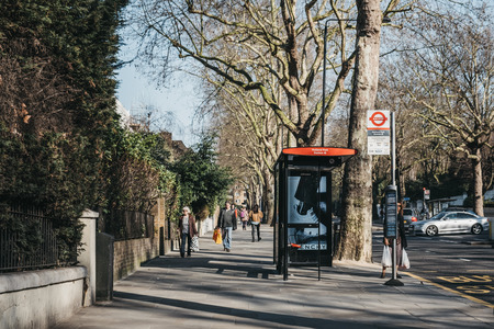 London, UK - February 23, 2019: Woman waiting for a bus in Holland Park, The Royal Borough of Kensington and Chelsea, on a sunny spring day. Holland Park is an affluent area in West London.のeditorial素材