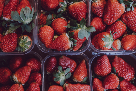 Top view of fresh strawberries on sale, portioned in plastic boxes, on top of a wooden tableの写真素材