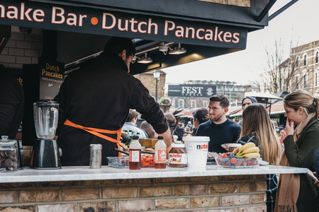 London, UK - March 23,2019: Staff cooking Dutch pancakes at a stall inside Camden Market, London. Started with 16 stalls in 1974, Camden Market is one of the busiest retail destinations in London.のeditorial素材