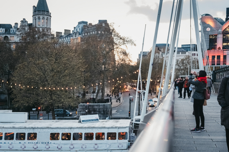 London, UK - April 13, 2019: Tourists taking pictures of London at dusk from Millennium Bridge, a steel suspension pedestrians bridge crossing the River Thames inking Bankside with the City of London.のeditorial素材