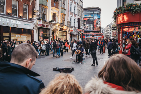 London, UK - April 13, 2019: People watching musician perform on a street in Chinatown, London....