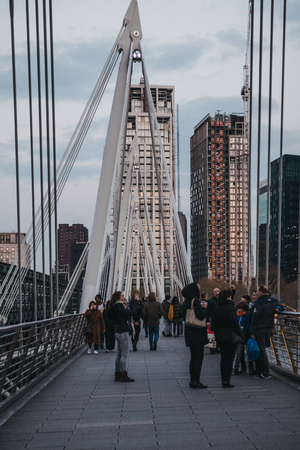 London, UK - April 13, 2019: Tourists taking pictures of London at dusk from Millennium Bridge, a steel suspension pedestrians bridge crossing the River Thames inking Bankside with the City of London.のeditorial素材