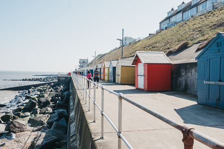 Sheringham, UK - April 21, 2019: People walking by colourful beach huts by the sea in Sheringham on a sunny day. Sheringham is an English seaside town within the county of Norfolk, UK.のeditorial素材