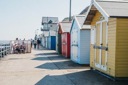 Sheringham, UK - April 21, 2019: People sitting by colourful beach huts by the sea in Sheringham on a sunny day. Sheringham is an English seaside town within the county of Norfolk, UK.のeditorial素材