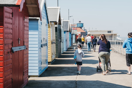 Sheringham, UK - April 21, 2019: Family walking by colourful beach huts by the sea in Sheringham on...