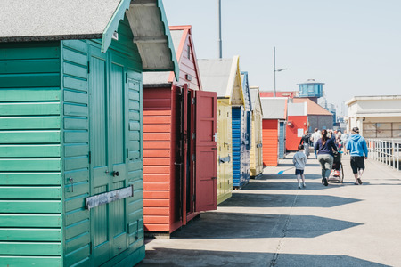 Sheringham, UK - April 21, 2019: Colourful beach huts by the sea in Sheringham on a sunny day, people walking on the background. Sheringham is an English seaside town within the county of Norfolk, UK.のeditorial素材